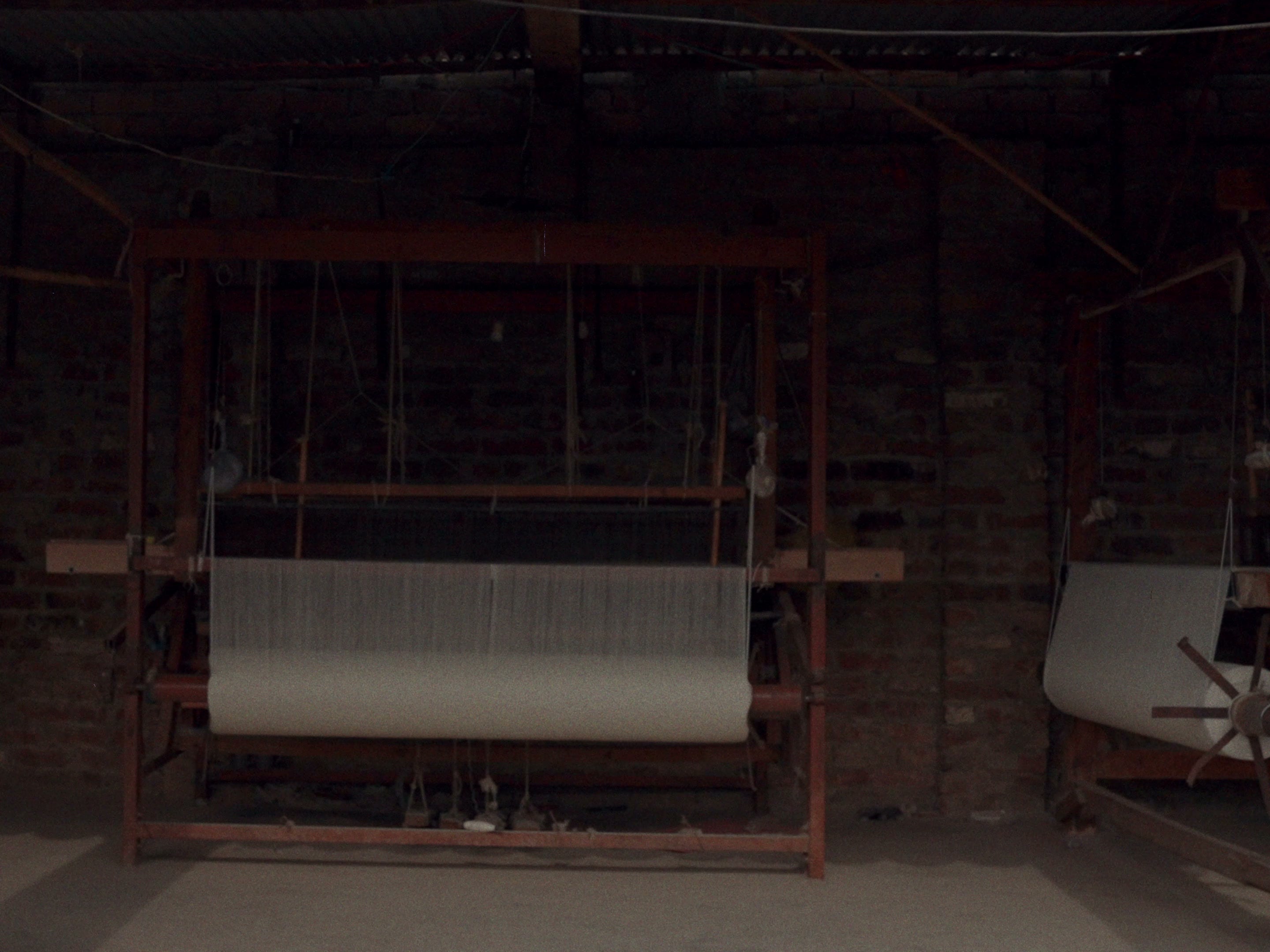 A wooden handloom in a dim workshop, warp stretched across the frame