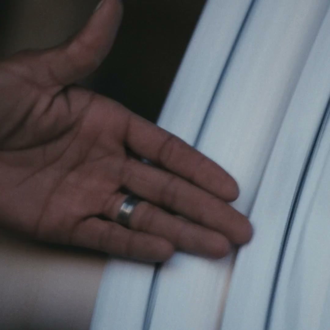 A weaver's open hand with a silver ring resting against a rolled bolt of pale handwoven wool cloth