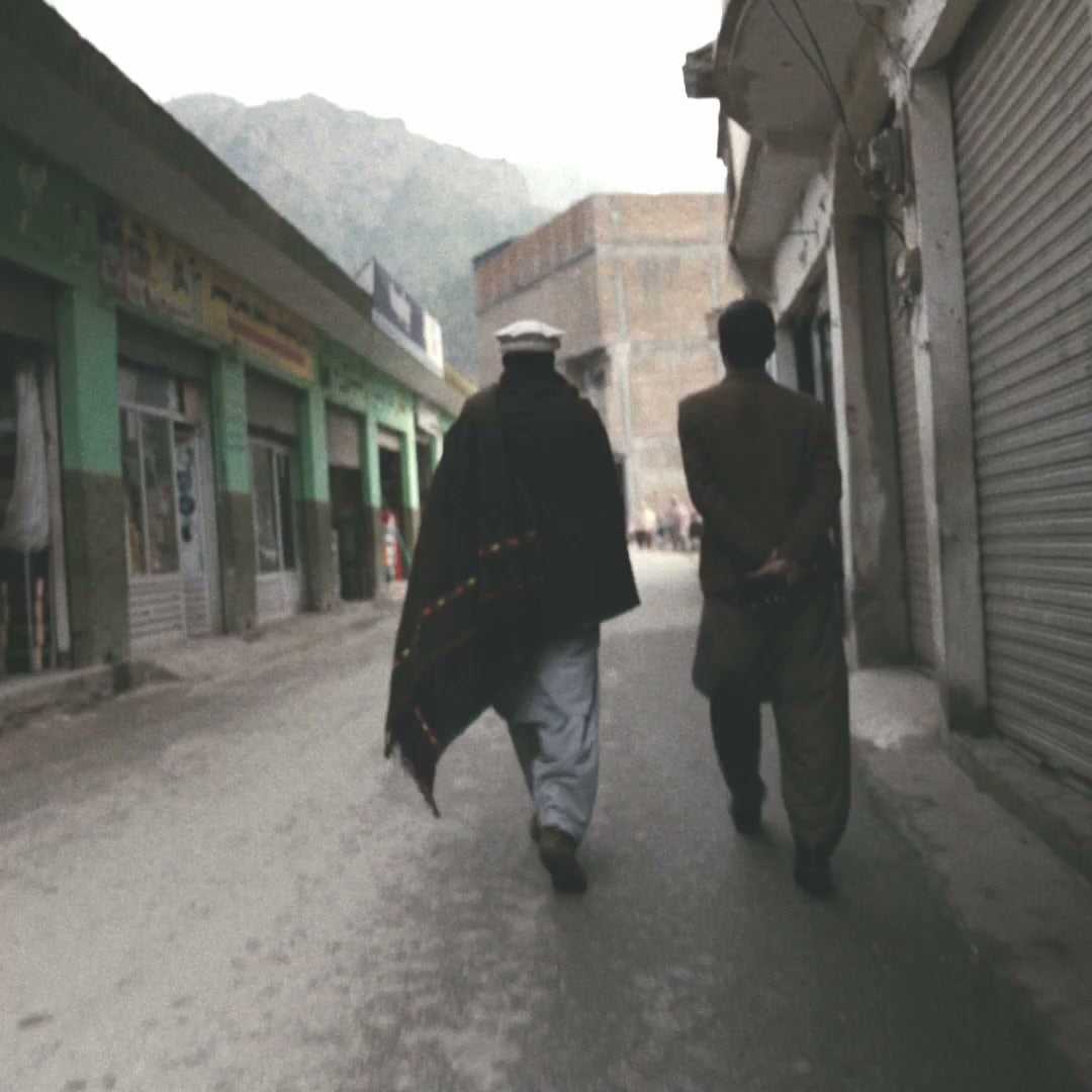 Two men in traditional wool shawls walking a misty bazaar street in Swat