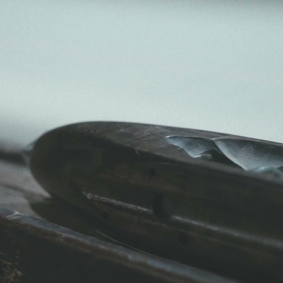 A carved dark-wood boat shuttle resting on the loom against a pale sky