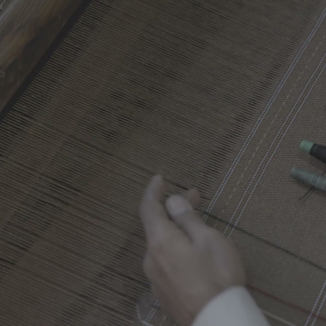 Overhead view of a hand weaving on the loom, woven cloth and two thread spools beside it